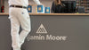 A contractor wearing white painter's pants with the Benjamin Moore logo on the back pocket, at a counter of a paint store with three gallons of Benjamin Moore REGAL select.